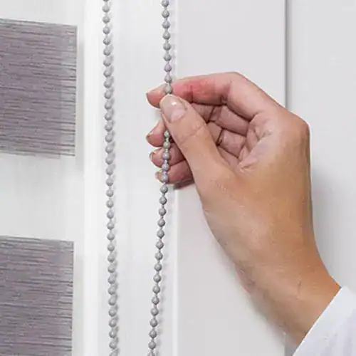 Close-up of hand adjusting beaded window blind chain.
