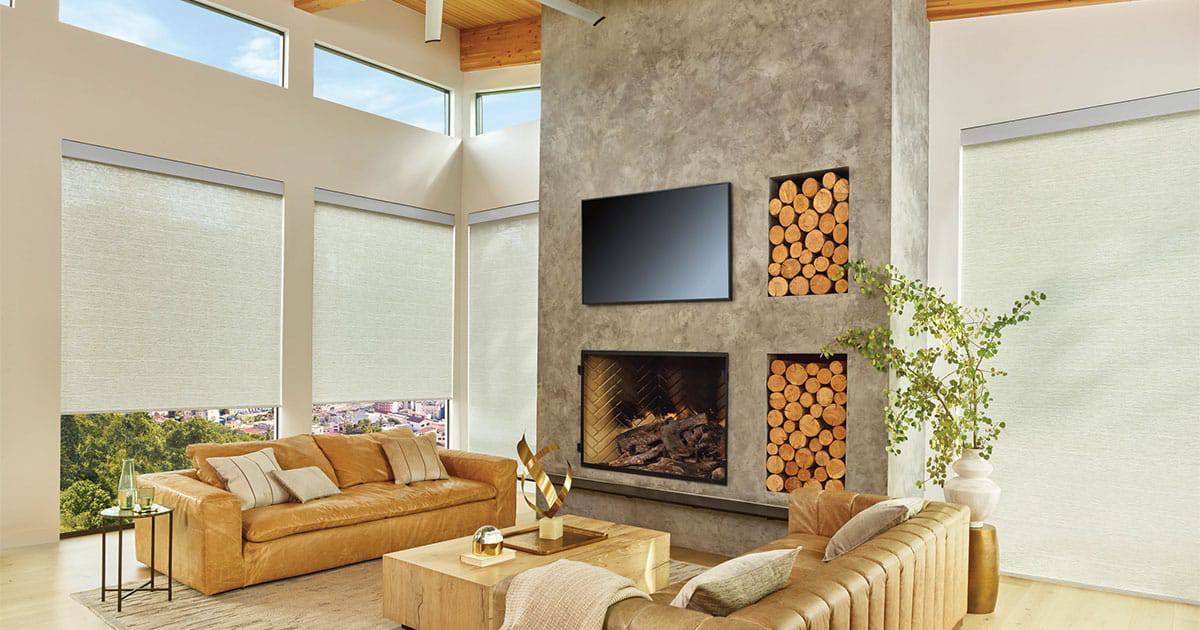 Bright living room with cozy fireplace, wood storage, large panoramic windows with blinds, and stylish leather sofas. Natural light floods the space, creating a warm and inviting atmosphere.