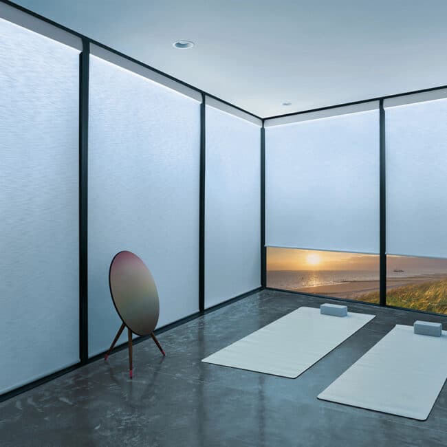 Bright modern yoga space with large windows and ocean sunset view, minimal decor, mats, blocks, and meditation accessories for relaxation and mindfulness.