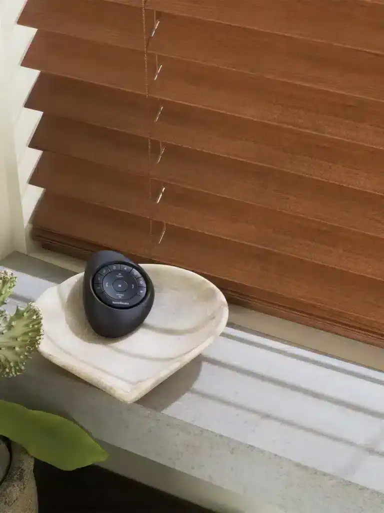 Black smart speaker on marble surface near wooden blinds, modern home decor.