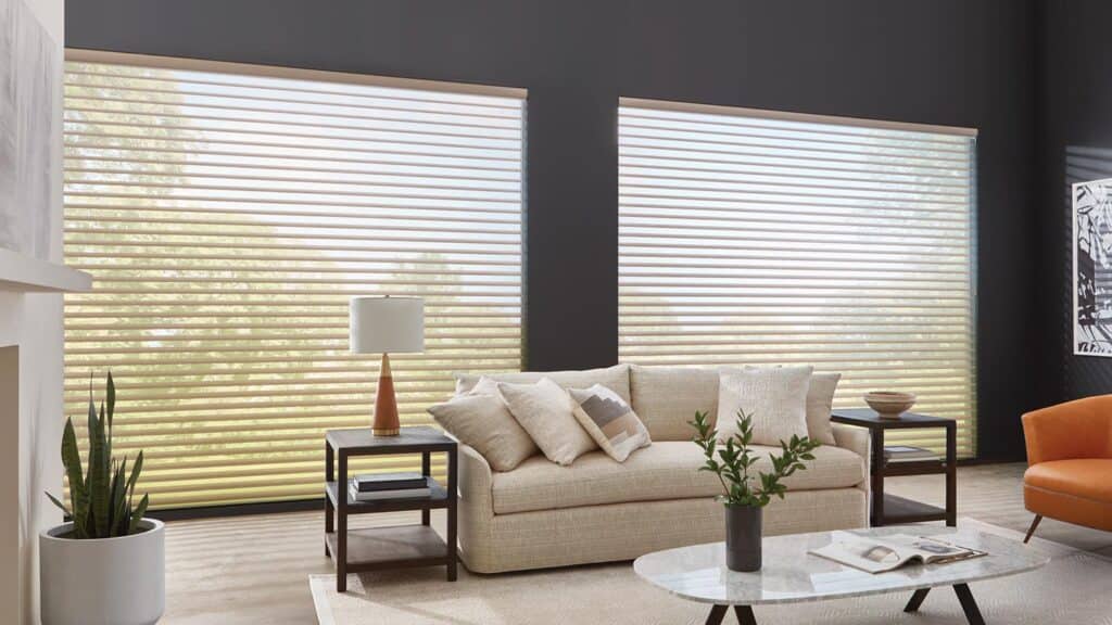 Bright living room featuring wide window blinds, neutral sofa, stylish side tables, houseplants, and contemporary decor.