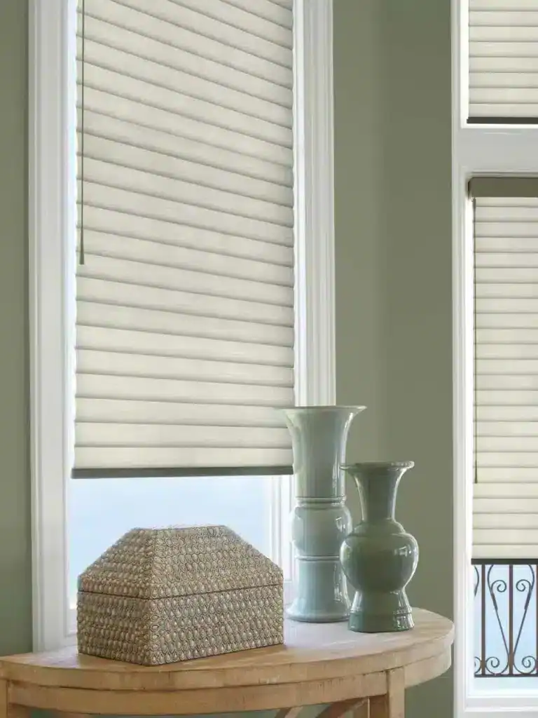 Bright interior window with stylish beige fabric blinds, natural light, white trim, decorative vases, elegant home decor, soft green wall, cozy ambiance, minimalist style, interior design inspiration.