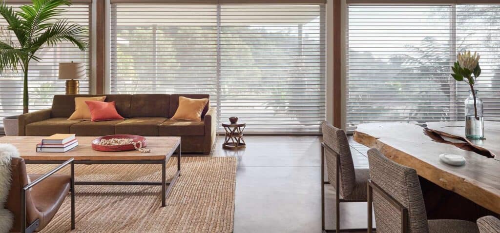 Bright living space featuring large windows with wooden blinds, a comfortable sofa with colorful pillows, and a blend of earthy and modern decor for a welcoming atmosphere.