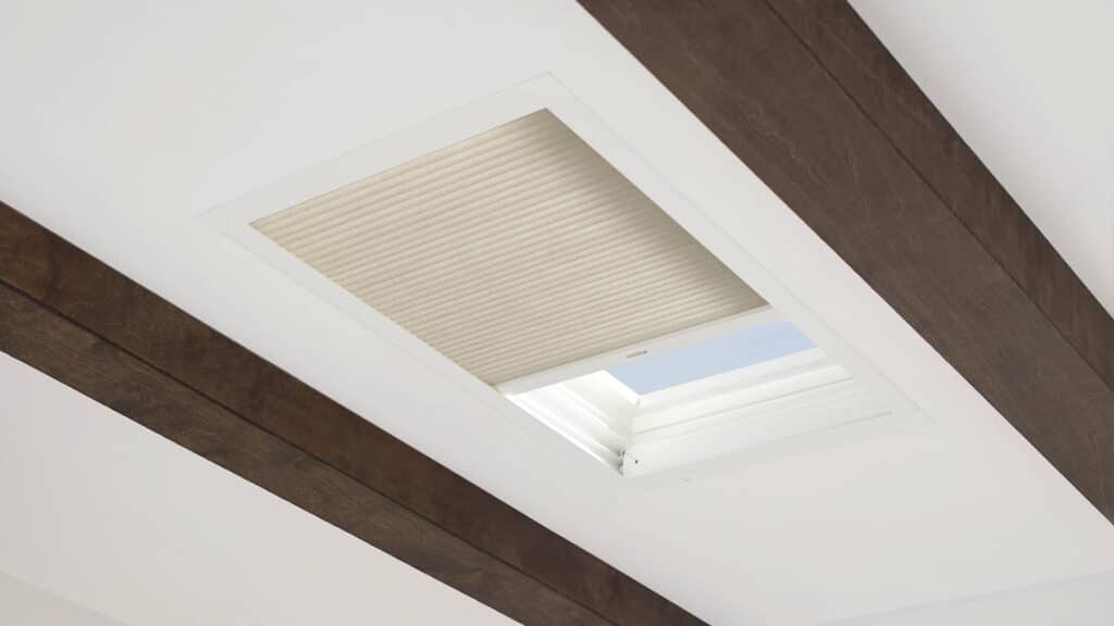 Bright skylight in ceiling with beige pleated shade, wooden beams accent, minimalist home decor, natural light, energy-efficient design.