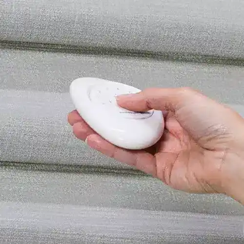 Close-up of a hand holding a white soap bar against a grey wooden background.