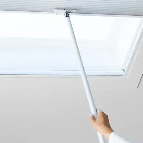A person using a long-handled tool to clean or maintain a ceiling or high window, demonstrating home or office ceiling cleaning or dusting.