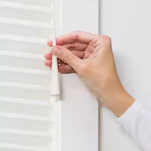 Close-up of a hand opening a white closet door with a handle.