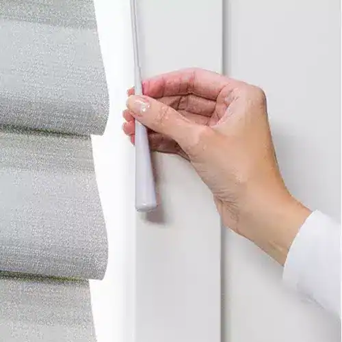 Close-up of hand adjusting simple white mini blinds window treatment.