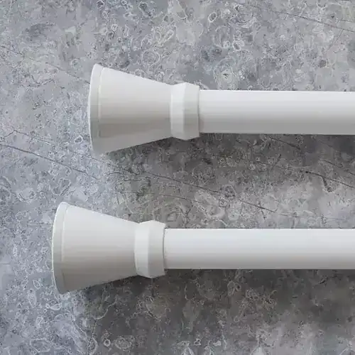 Two white curtain rods with finials on a gray textured surface, ready for installation in a modern home interior.