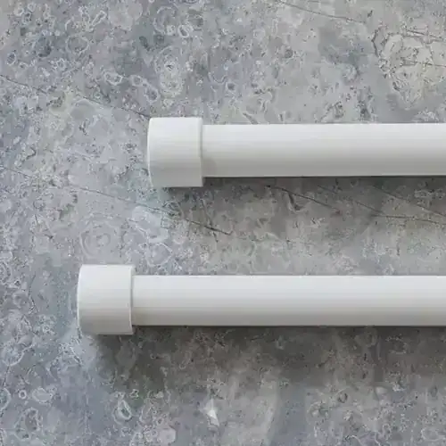 Two white curtain rods placed parallel on a gray textured floor, showing their cylindrical shape and simple design.