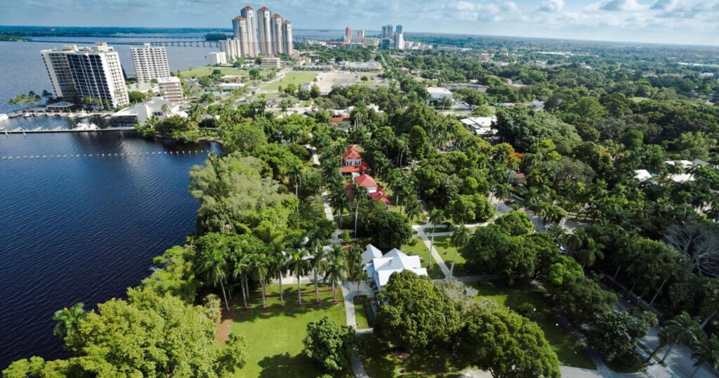 Aerial view of Lee County showing a mix of high-rise buildings, residential areas, and lush green parks near a large water body.