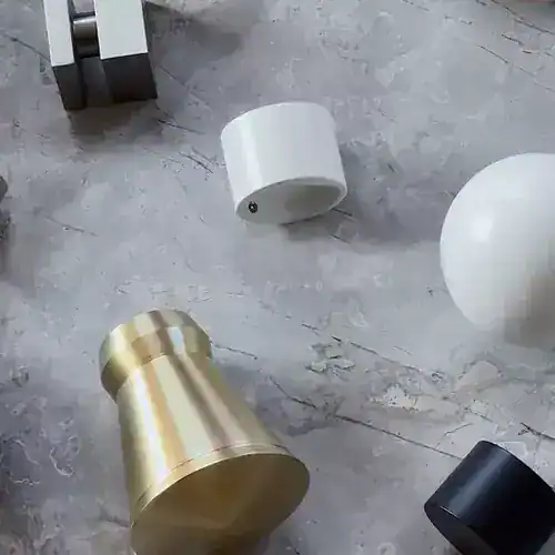 Collection of stylish vases and spherical decor pieces on a textured concrete surface, including a gold vase, white and black spheres, and a white cylindrical container.