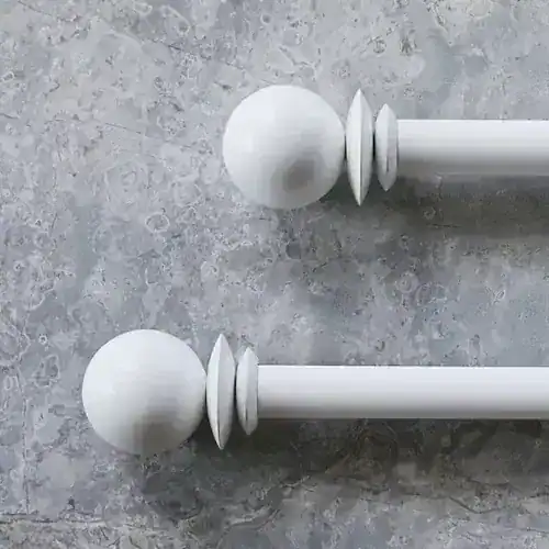 Two white curtain rods with round finials on a textured gray background, close-up view.