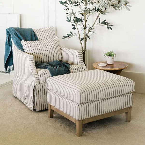 Elegant striped upholstered armchair with matching ottoman in a cozy living room setting, complemented by a small side table and indoor plant.