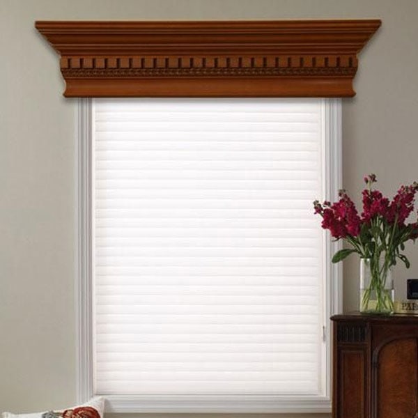 White window blind with a decorative wooden valance in a home interior, featuring a vase of pink flowers on a wooden side table.