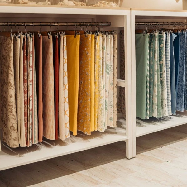 Colorful selection of designer fabrics hanging on a rack in a fabric store, showcasing various patterns and textures for home decor and fashion.