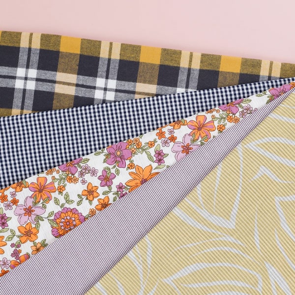 Close-up of various designer fabrics with different patterns and colors, including plaid, gingham, floral, and geometric designs.