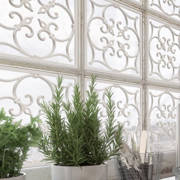 Close-up of ornate white metal grilles with intricate scrollwork design, used as decorative window panels.