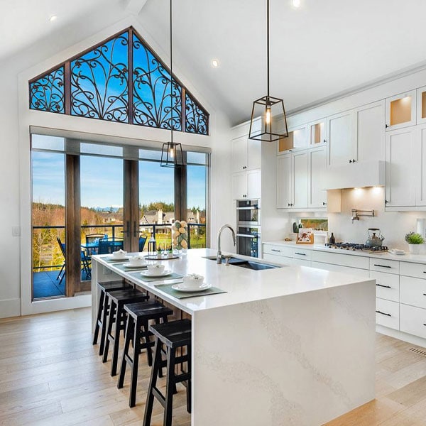 Elegant kitchen with decorative iron grille panel above large sliding glass doors, white cabinetry, and modern island with seating.
