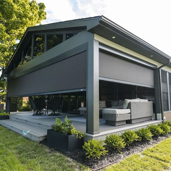 Contemporary two-story house with large outdoor deck, glass windows, and modern furniture, surrounded by greenery and landscaping.